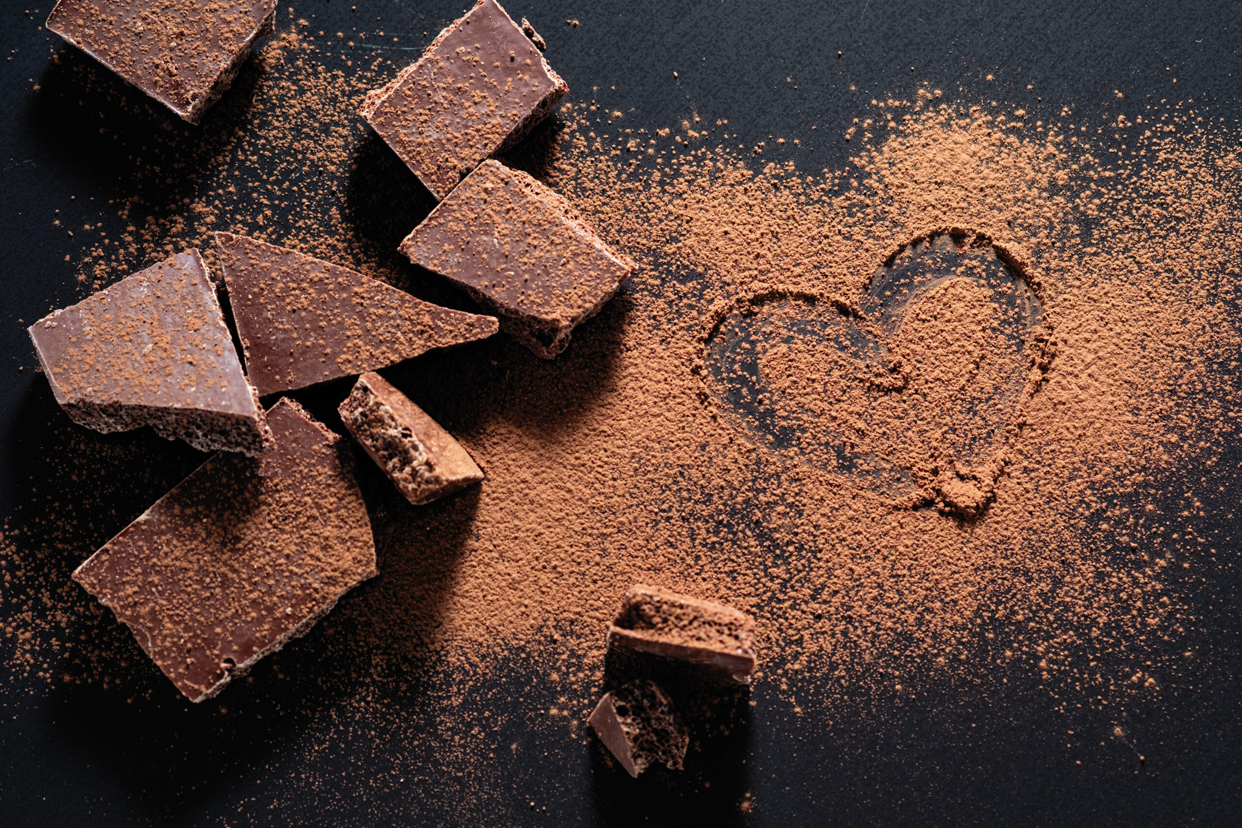 broken chocolate bar on a black background, cocoa powder painted heart
